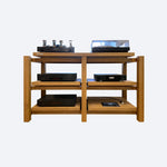 A wooden audio rack with two shelves, the top shelf holding a hifi turntable and lamp amplifier, and other audio equipment, and the bottom shelf holding speakers.