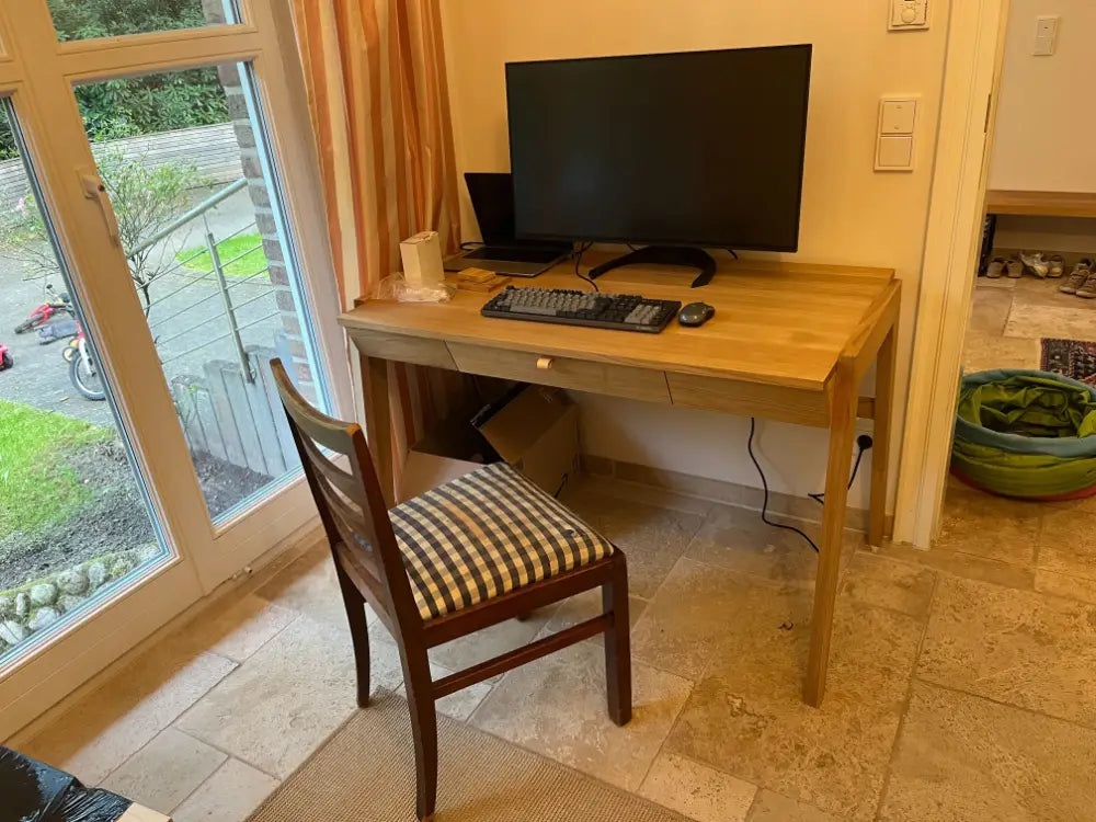 Premium desk with drawer handmade of solid wood standing on stone floor in living room next to big window