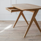 Kunsst real wood vintage desk with drawer placed in a bright living room with warm oak flooring. The white wall behind features  elegant moulding. 
