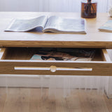 Solid wood vintage desk with drawer with an open book on oak desk top and a magazine inside a drawer, on a light wooden floor standing in front of window