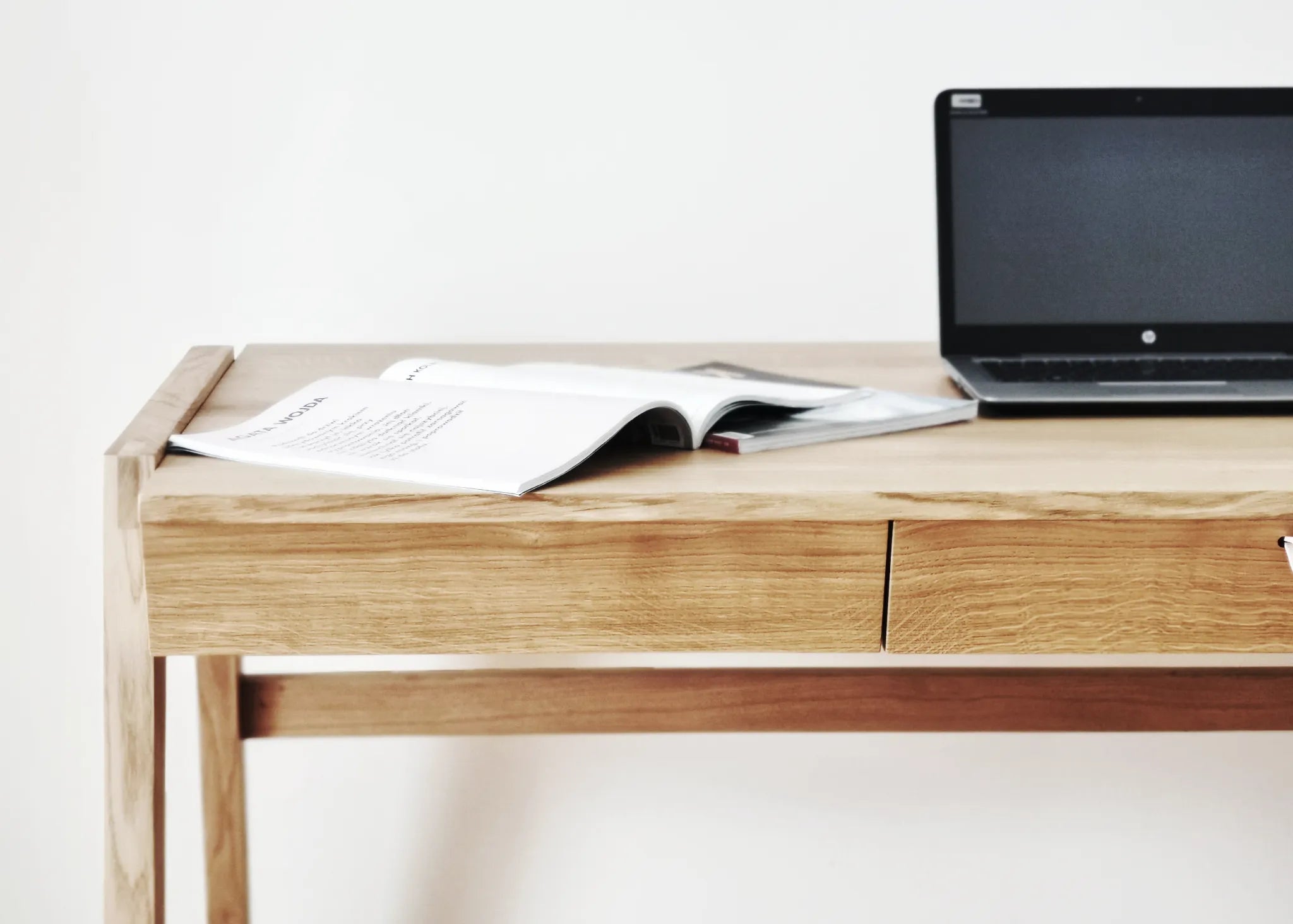 Front view of luxury real wood desk with drawer with a laptop and open book on oak desk top standing on a white background