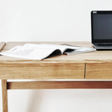 Front view of luxury real wood desk with drawer with a laptop and open book on oak desk top standing on a white background