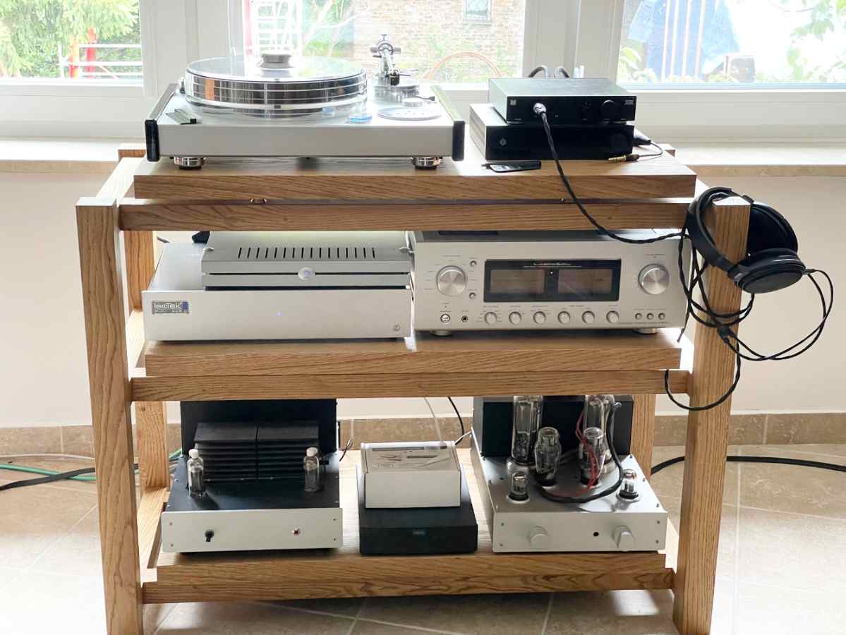 Kunsst wooden hi-fi audio rack  supporting a McIntosh amplifier and turntable, placed in an audiophile room next to a large window.