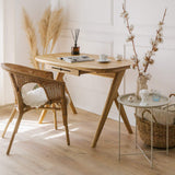 Small solid wood desk for vanity is showcased in a luxury living room with wicker chair and decorative items in a bright room with elegant mouldings. Magazine and cup of coffee laying on rounded corners desk top. 