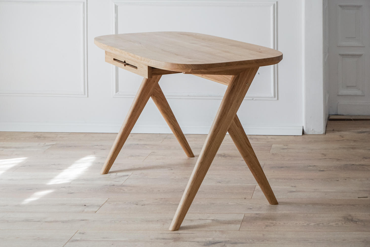 Kunsst mid century modern desk for small spaces placed in a elegant living room with warm wooden flooring. The white wall behind features  classic moulding.