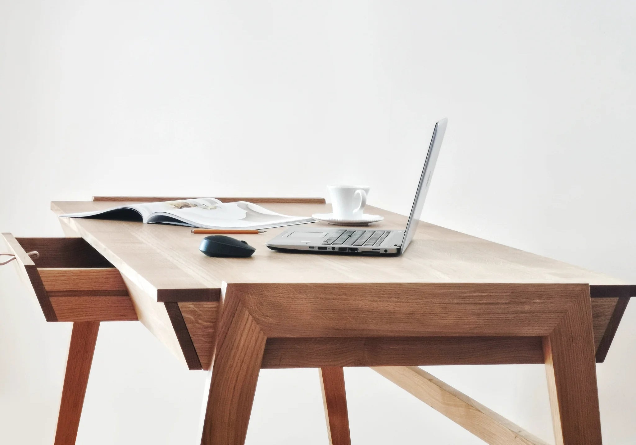 Solid wood desk with drawer standing on white background with MacBook and magazine on oak desktop