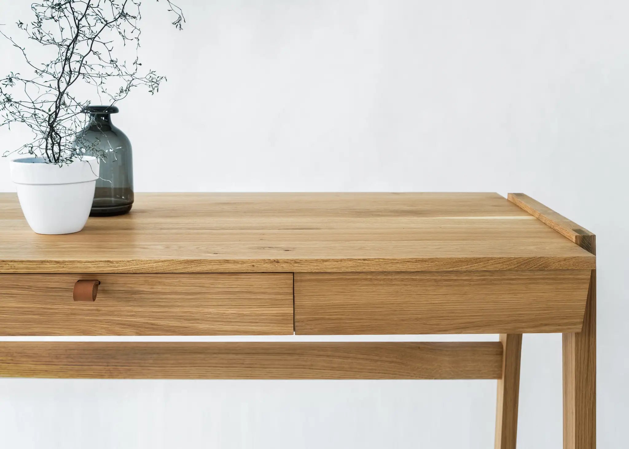 Front view of real wood desk with drawers with  vase and branches on solid oak desk top standing in front of a white background