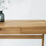Front view of real wood desk with drawers with  vase and branches on solid oak desk top standing in front of a white background