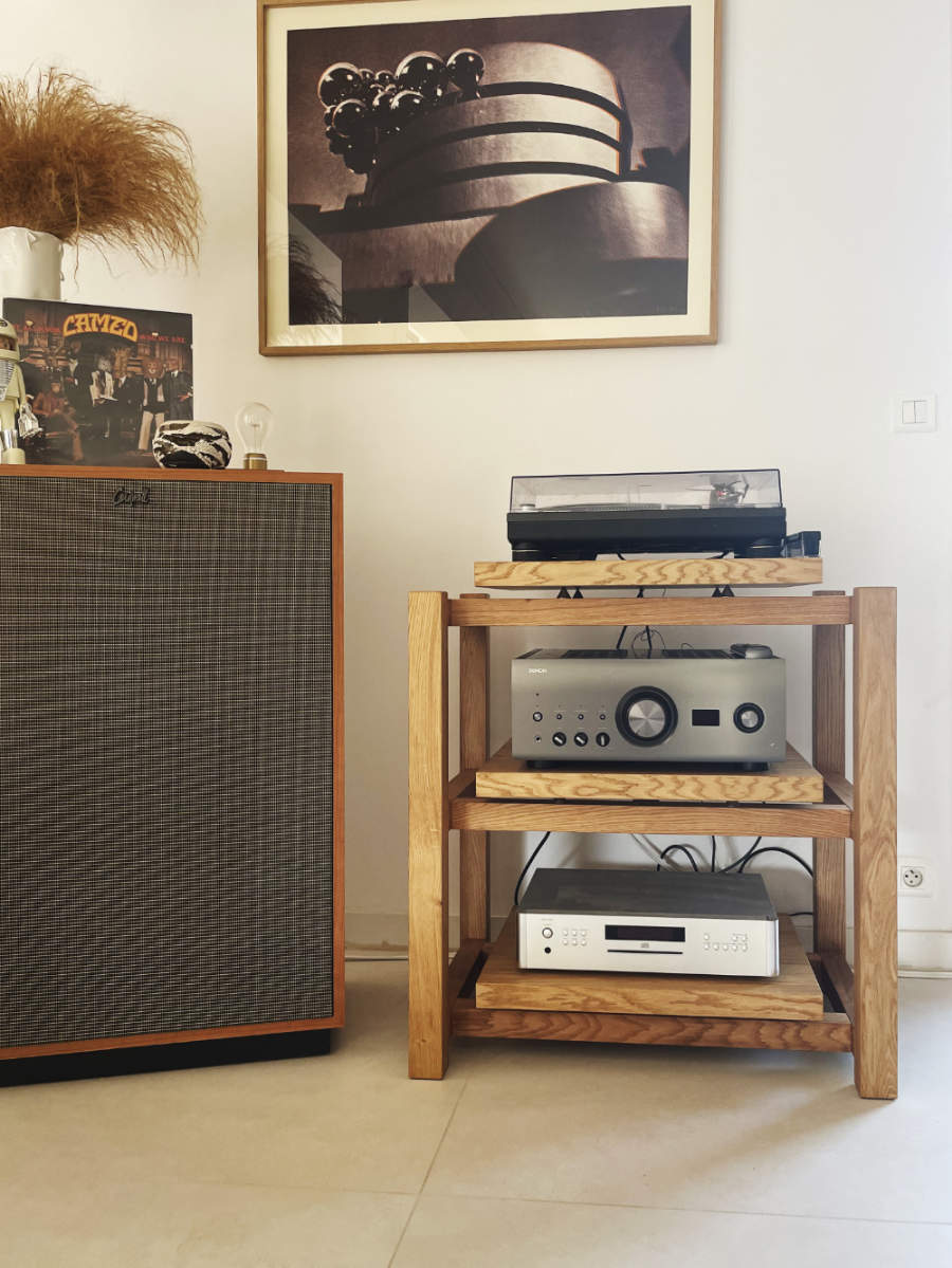 A turntable on a wooden audio table, with a Denon PMA-A110 amplifier and a Rotel CD player on the shelf below