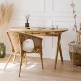 Elegant solid wood vintage desk for a vanity with wicker chair and decorative items, standing on a wooden floor in a classic style room with wall mouldings.