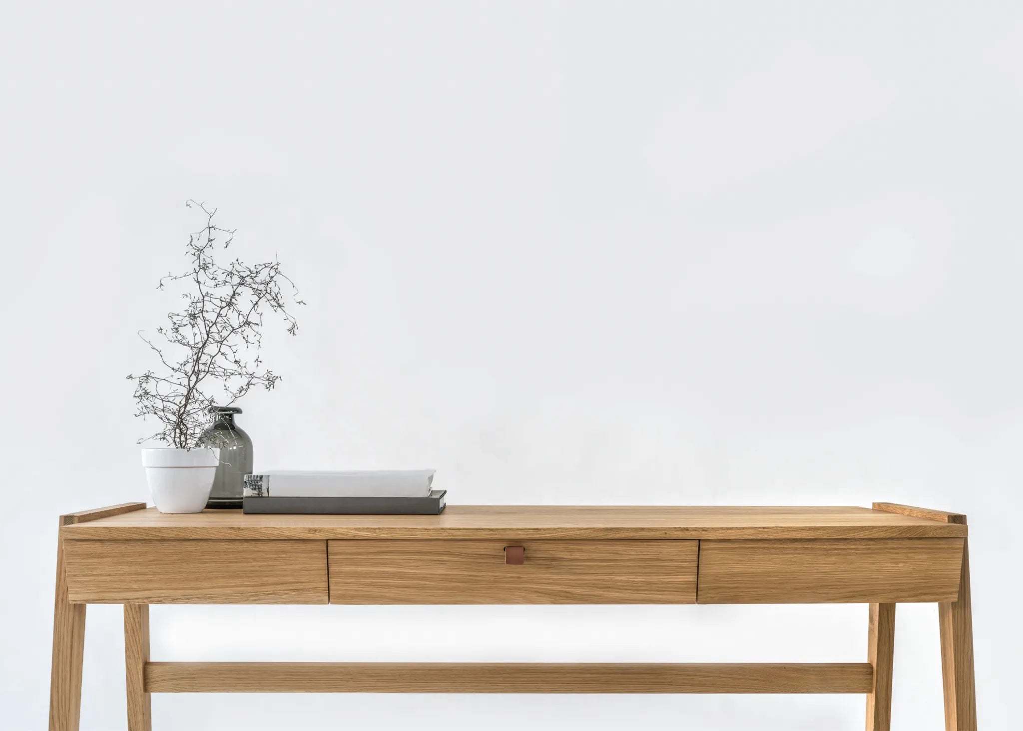 Front view of solid wood desk with drawer, crafted from solid oak with a vase and branches a white background
